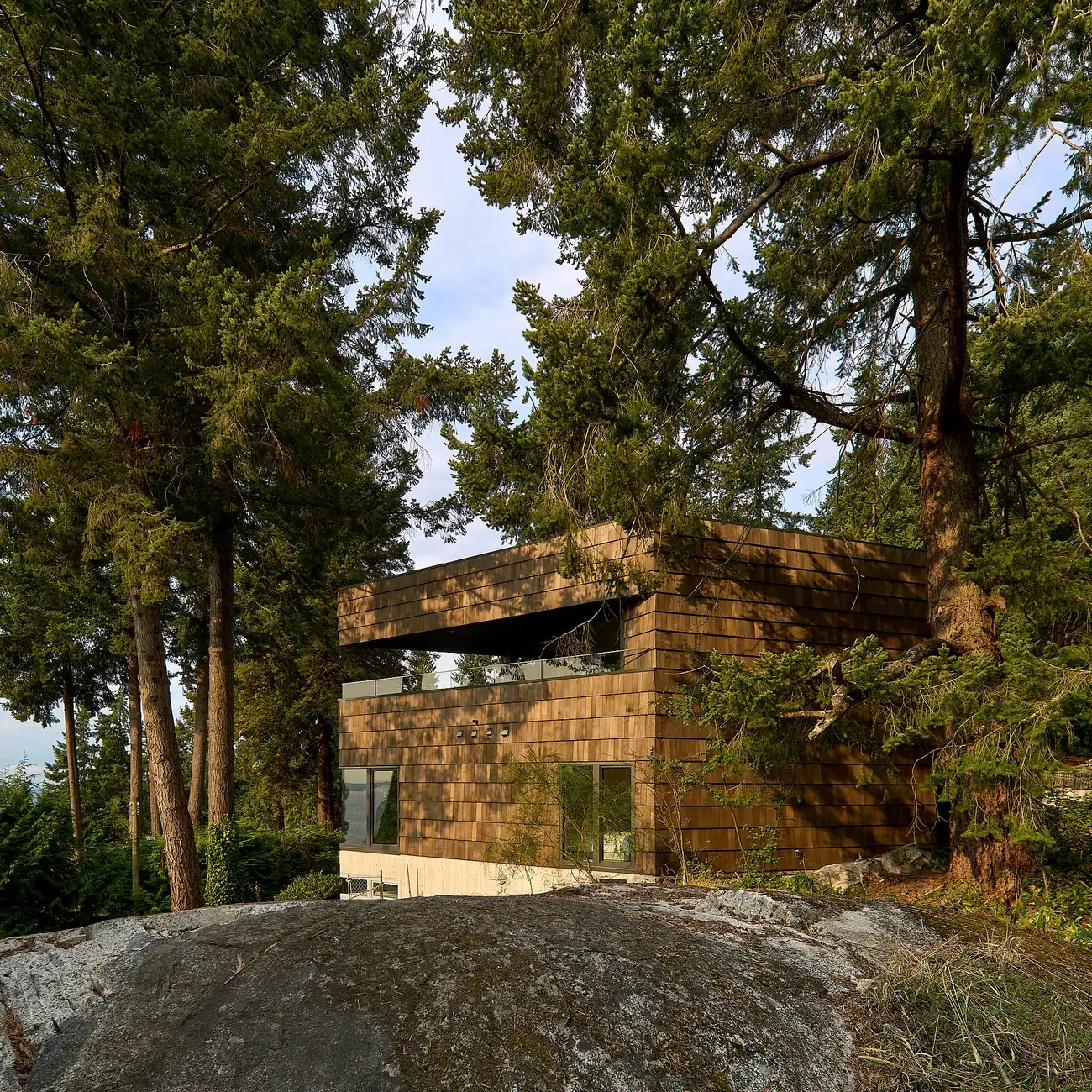 The shingled Rose house among mature trees, natural rock and coastal landscape