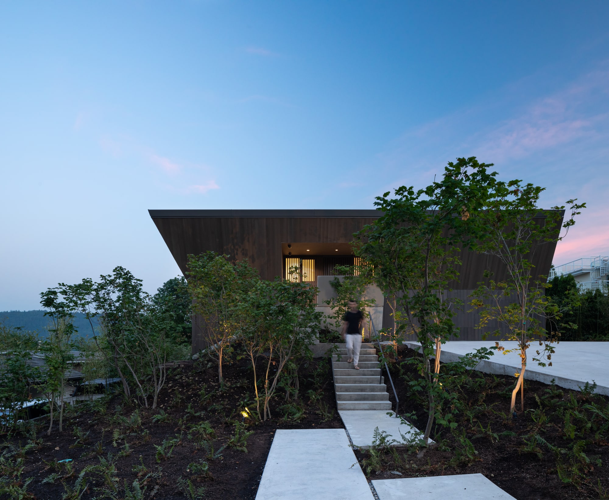 Deep Cove House — A person descending the front entrance steps beneath the projecting roof at dusk