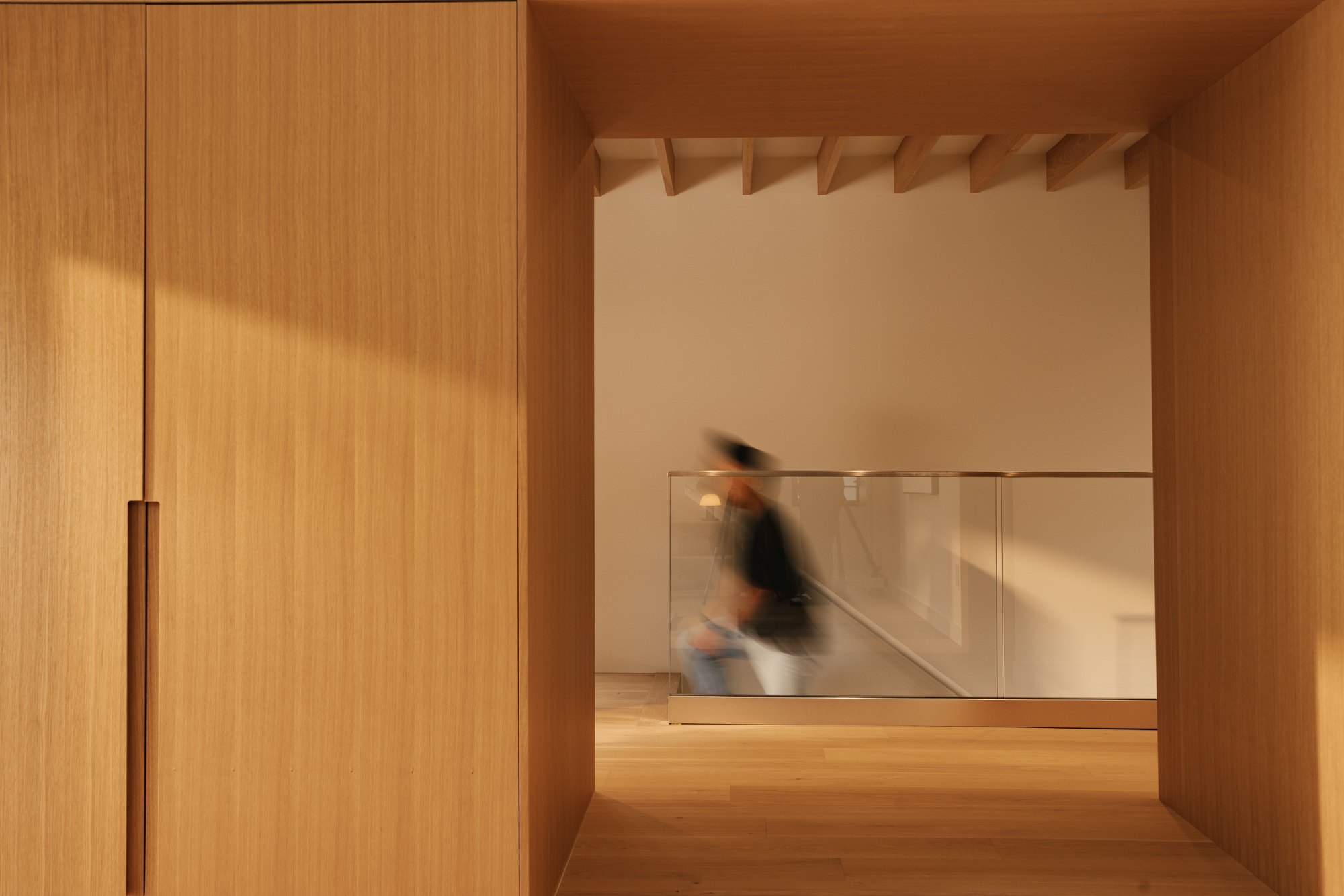 A person crossing the upper walkway beyond a timber-lined opening.